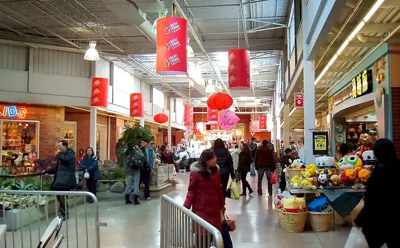 a crowded indoor shopping mall with red lanterns and banners hanging from the ceiling, people walking through aisles, and a…