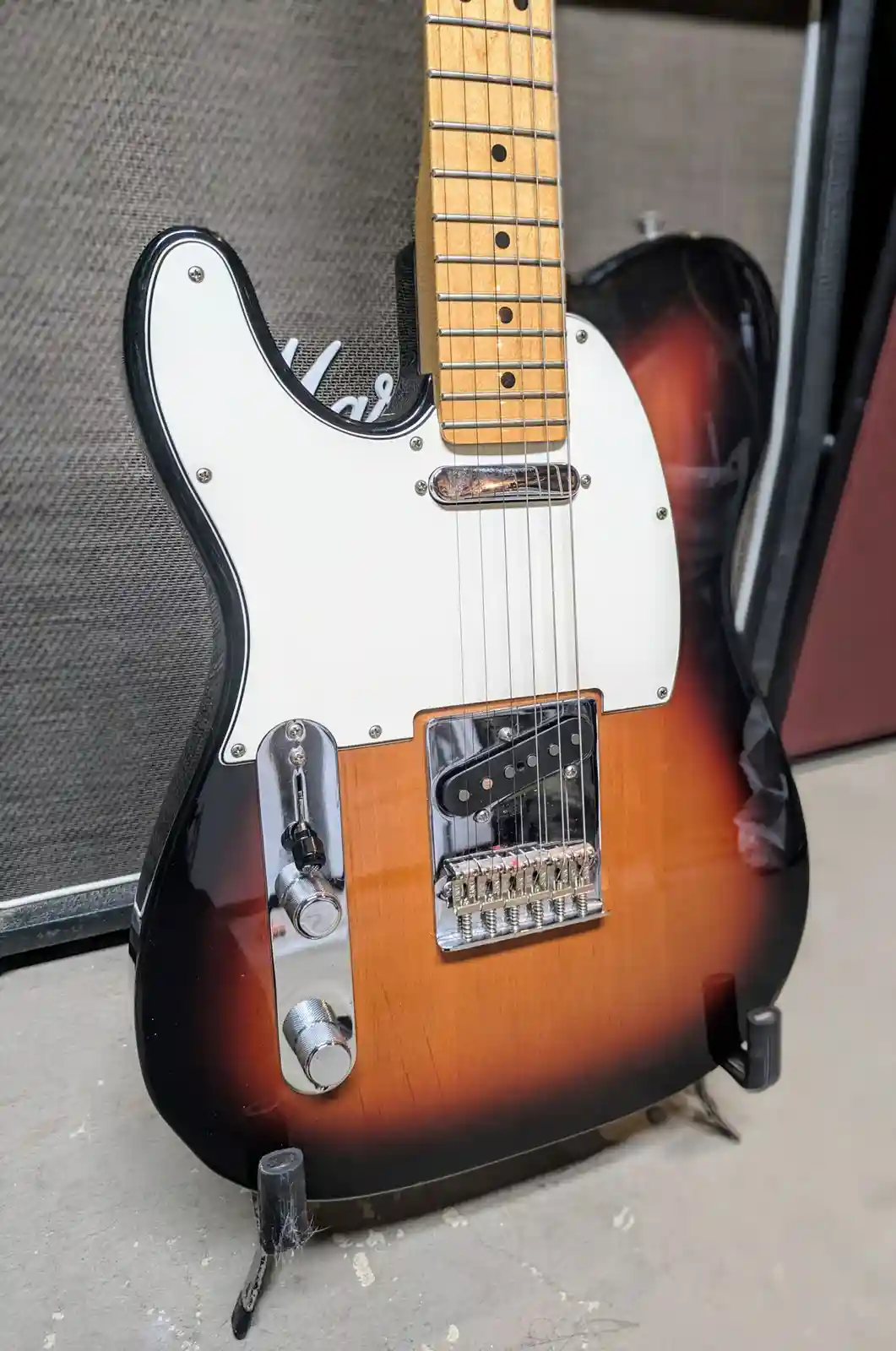 A close-up photo of a sunburst-finish electric guitar, likely a Fender Telecaster, standing upright on a stand against a…