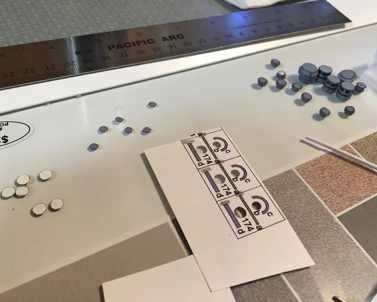 A close-up photo shows a model kit decal sheet with three identical blue circular decals labeled '174' and 'c', surrounded…