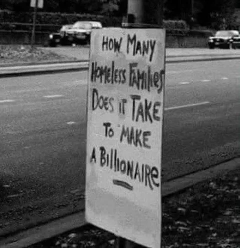 A black-and-white photo shows a handmade sign posted on a roadside, asking 'HOW MANY HOMELESS FAMILIES DOES IT TAKE TO MAKE…