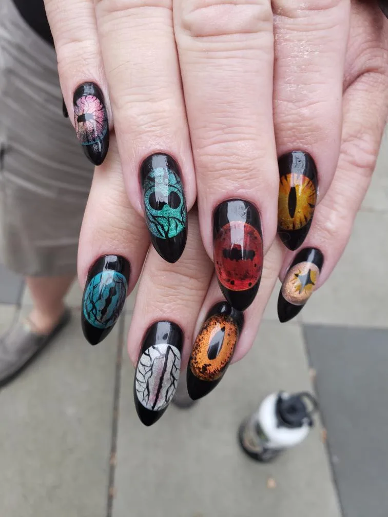 A close-up photo shows a person's hands with long, black stiletto nails, each decorated with a different intricate design…