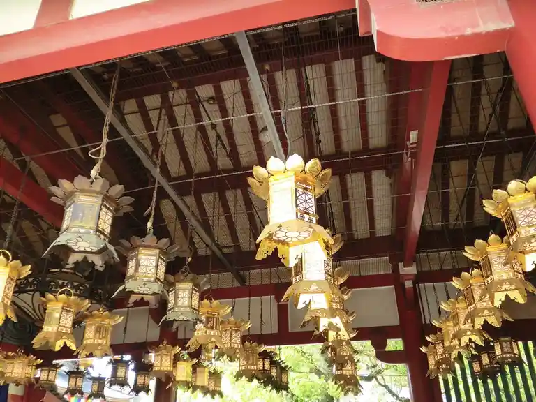 The image shows numerous ornate, traditional Japanese lanterns hanging from a red wooden ceiling structure with exposed…