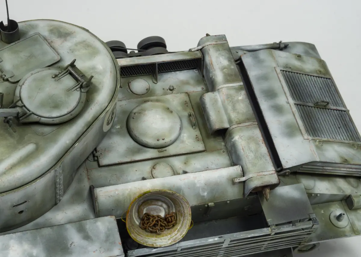 A close-up photo of a detailed, weathered model tank's top surface, showing hatches, vents, and a small metal bowl filled…