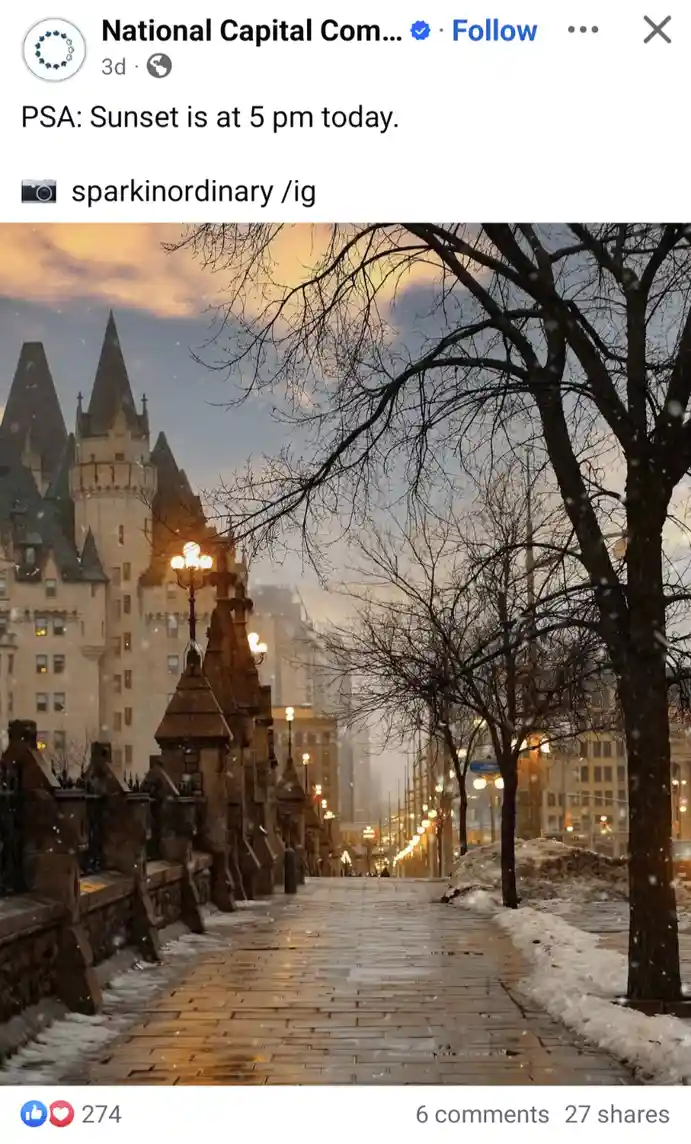 A snowy, atmospheric street scene at dusk with a grand castle-like building on the left, bare trees, and illuminated street…