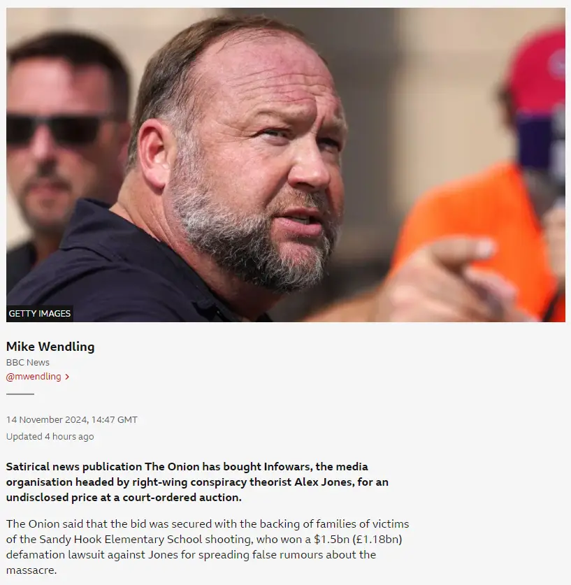 A close-up photo of a man with a beard and receding hairline, wearing a dark shirt and pointing forward with his right hand…