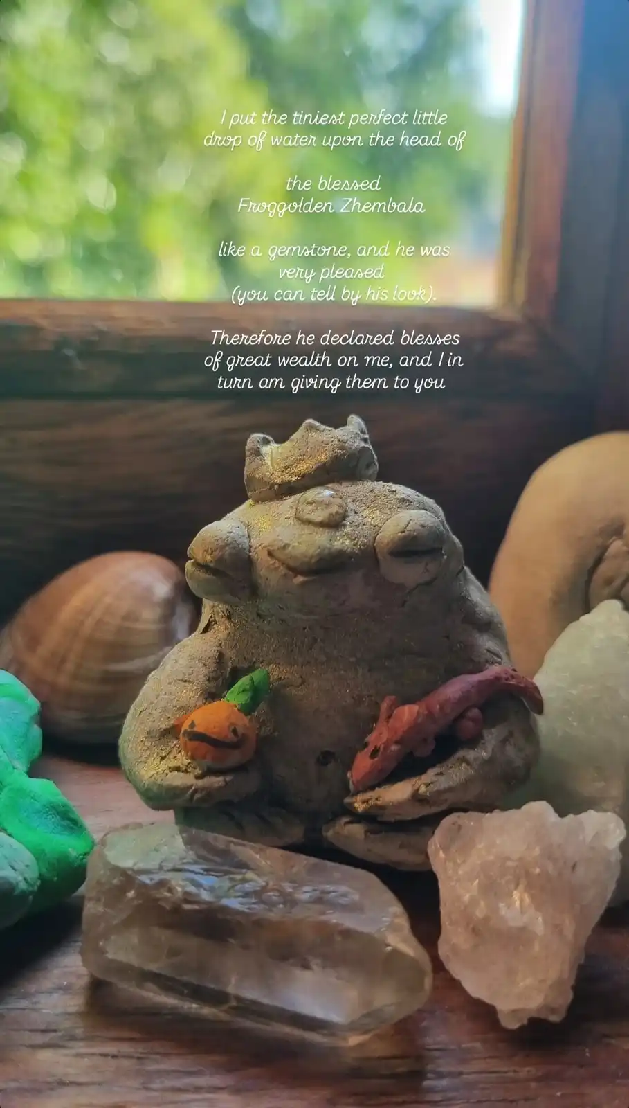 A ceramic frog figurine, adorned with a tiny crown and holding small clay figures, sits on a wooden surface surrounded by…