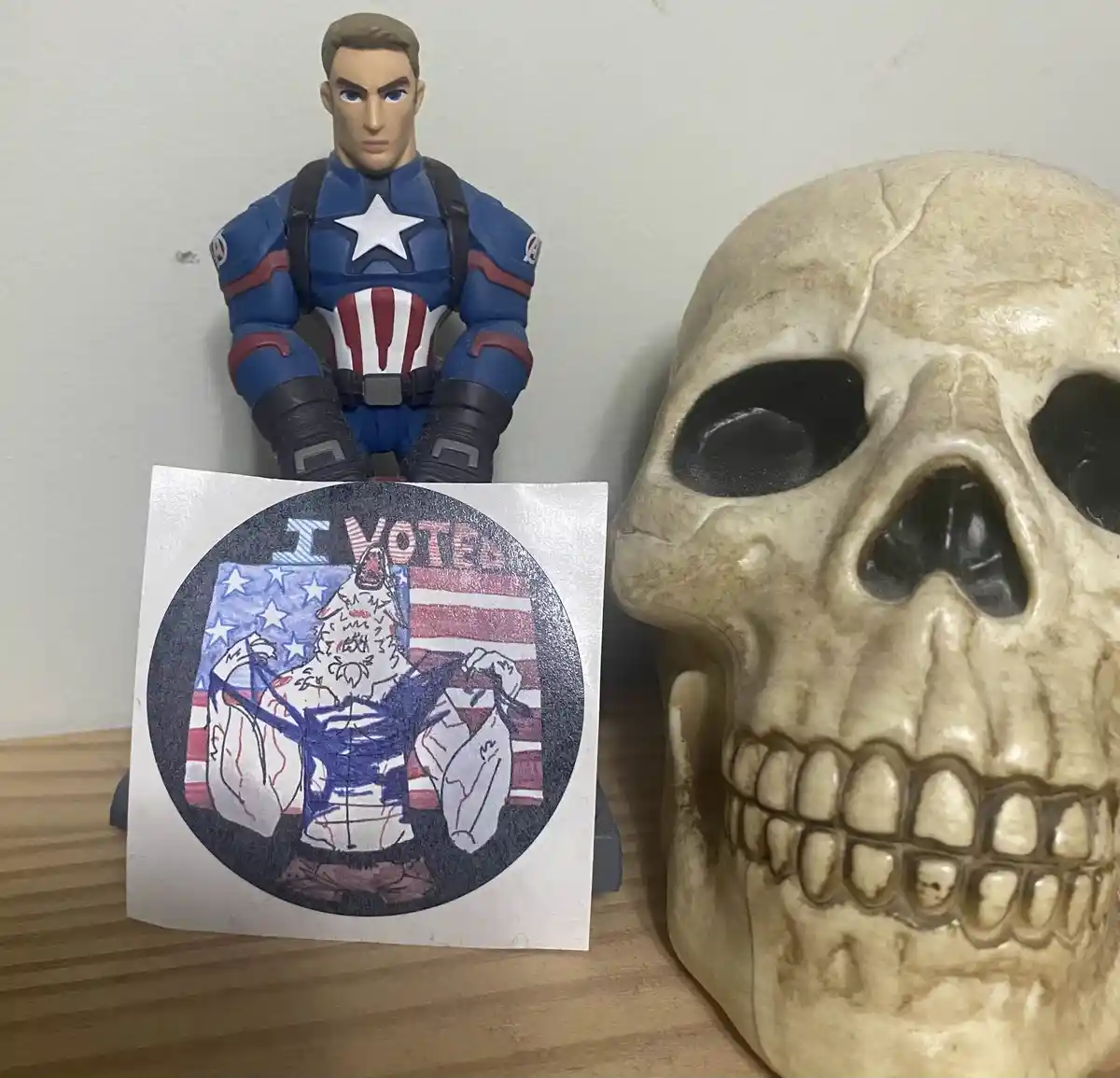 A Captain America action figure stands next to a human skull, holding a custom 'I VOTED' sticker featuring a cartoon wolf in…