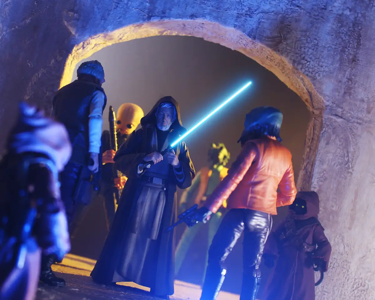 A group of Star Wars action figures, including a Jedi with a blue lightsaber, stand in a stone archway. The central figure…