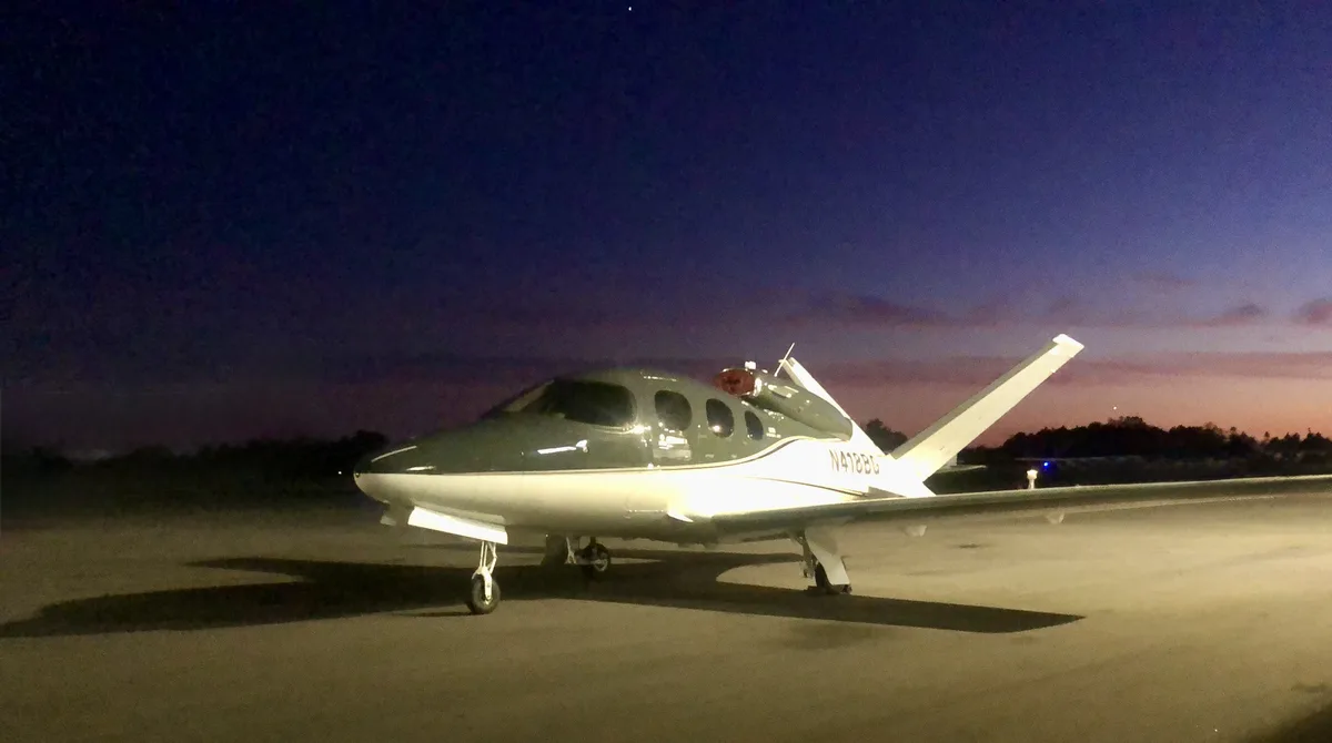 A small private airplane with the registration number N418BG is parked on a tarmac at dusk or dawn, with a dark sky and…