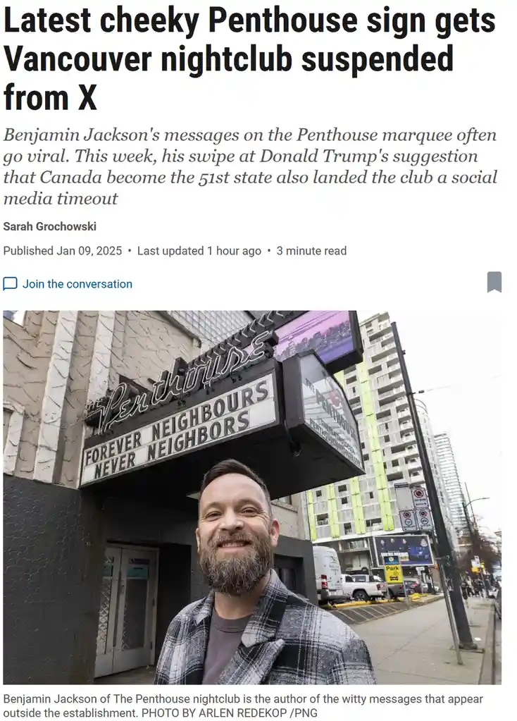 A man with a beard and plaid jacket stands smiling in front of a nightclub called 'The Penthouse'. The marquee above him…