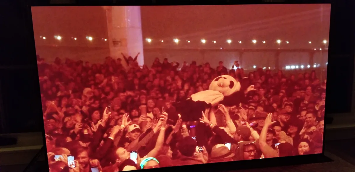 A large crowd at a concert or event is shown on a screen, enthusiastically lifting a person in a large, round…