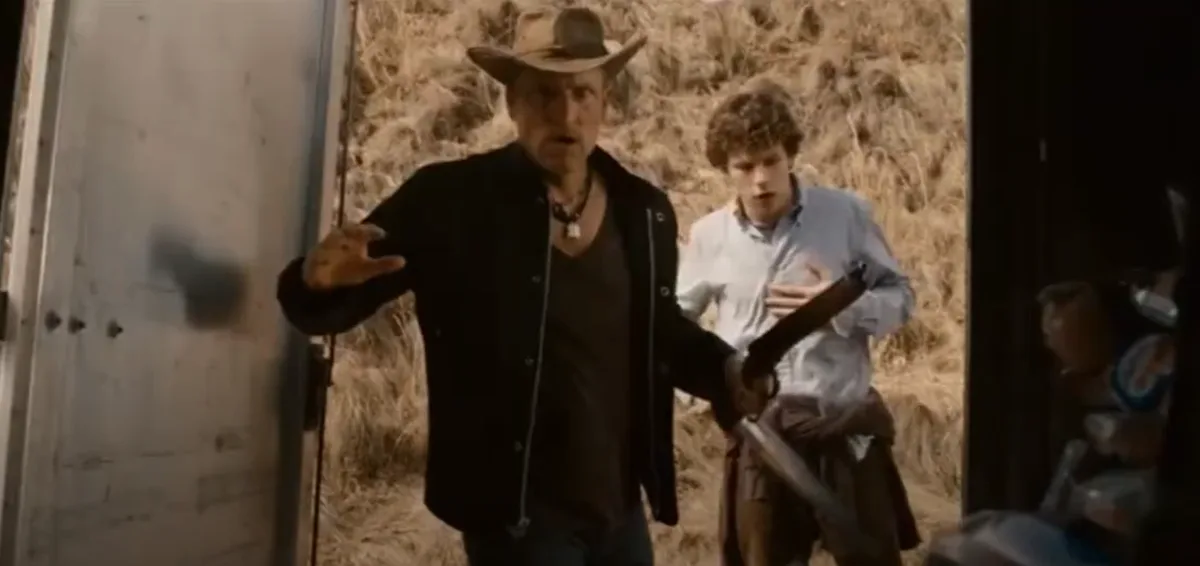 A man in a cowboy hat and black jacket stands in a doorway with a shocked expression, holding a rifle, while a younger boy…