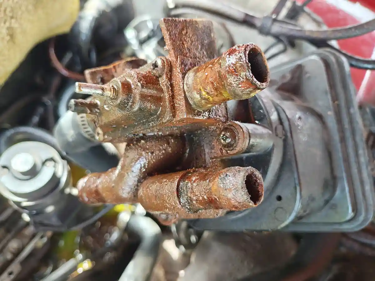 A close-up photo shows a heavily rusted, corroded automotive part, likely a carburetor or fuel line connector, with visible…