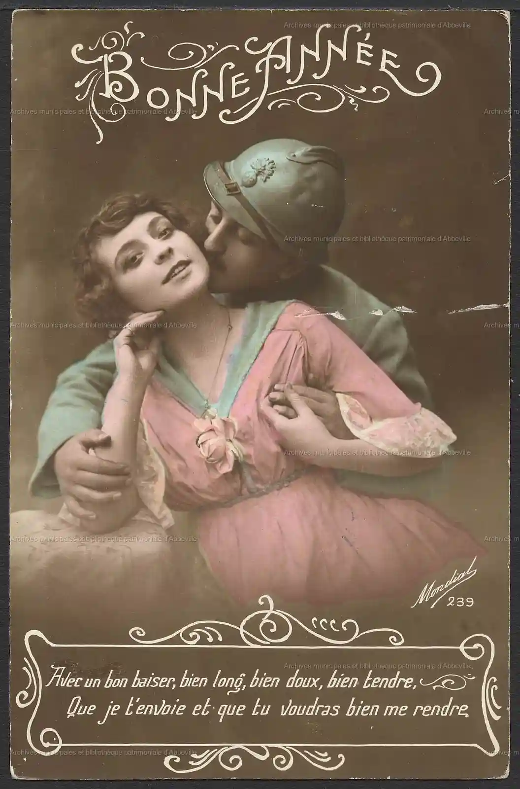 An old French New Year's greeting postcard shows a soldier in a helmet kissing a woman in a pink dress. The ornate text at…