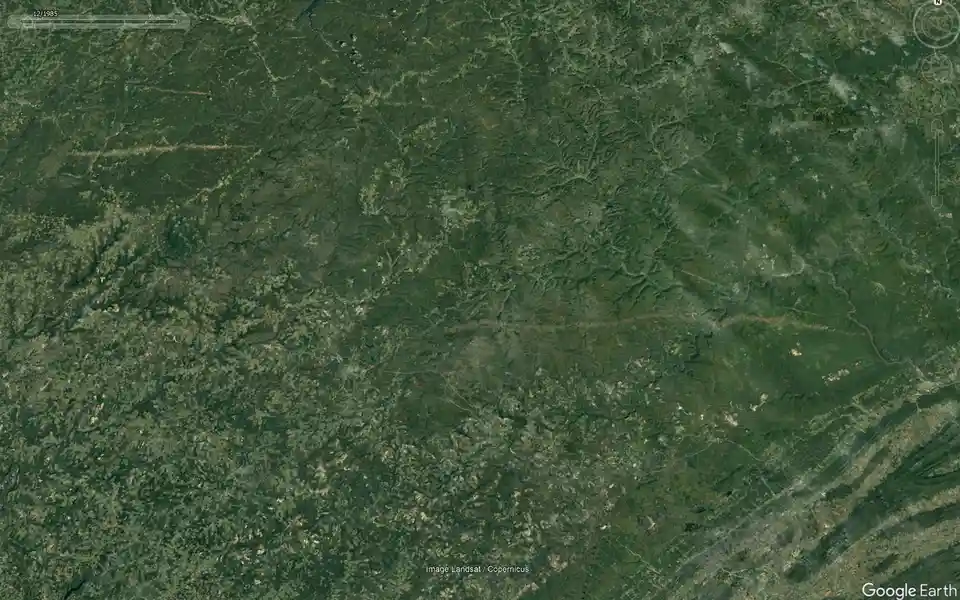 A satellite view of a green, forested, mountainous terrain with winding rivers and scattered settlements, overlaid with the…