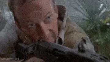 A man aims a rifle in a jungle setting, then the camera pans to reveal a giraffe behind him. He then looks back at the…