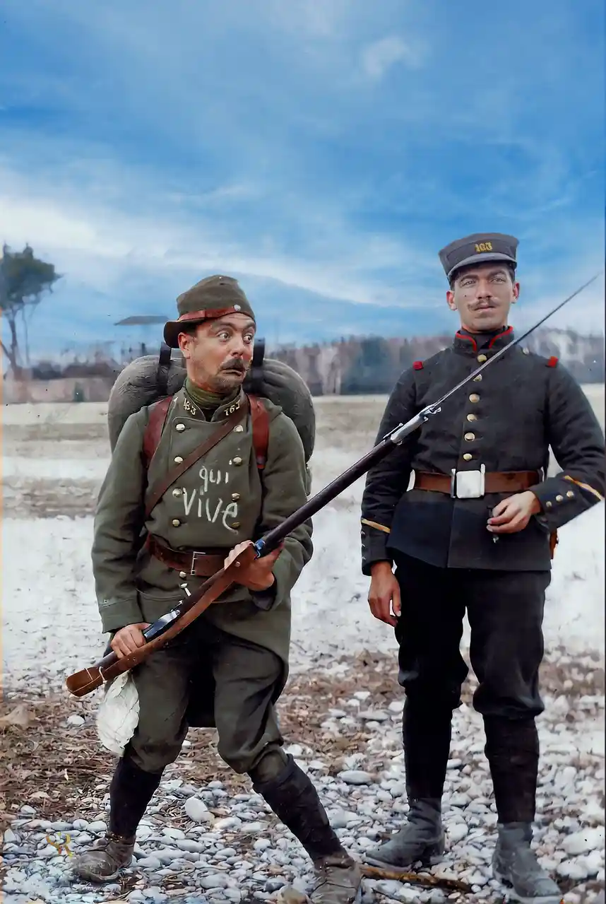 Two soldiers in early 20th-century military uniforms stand in a rocky field under a blue sky. The soldier on the left, in a…