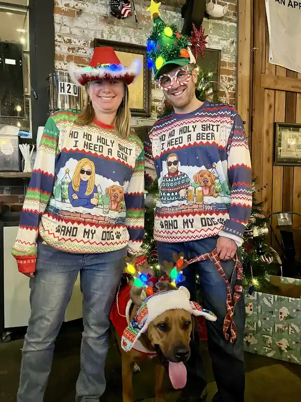 A man and woman stand together wearing matching ugly Christmas sweaters featuring cartoon characters and the text 'HO HO…