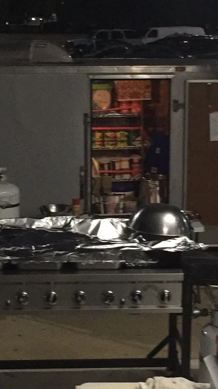 A nighttime photo shows a large outdoor grill covered in aluminum foil with a metal dome lid, positioned in front of an open…