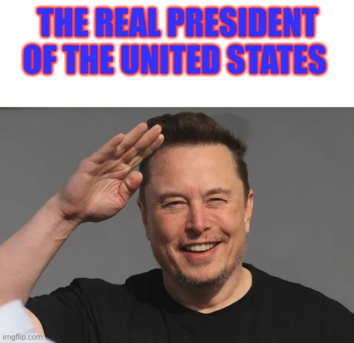 A man with dark hair and a beard, wearing a black t-shirt, smiles broadly while raising his right hand in a salute gesture…