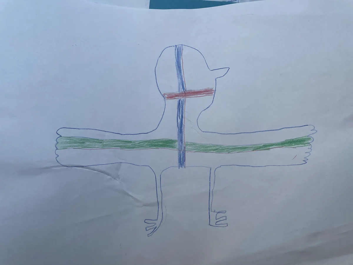 A child's crayon drawing on white paper shows a simple blue outline of a figure with a round head, stick arms, and legs. A…