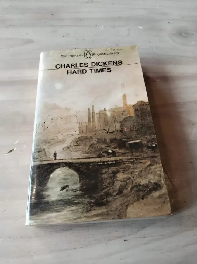 A physical copy of Charles Dickens' novel 'Hard Times' from The Penguin English Library, featuring a sepia-toned cover…