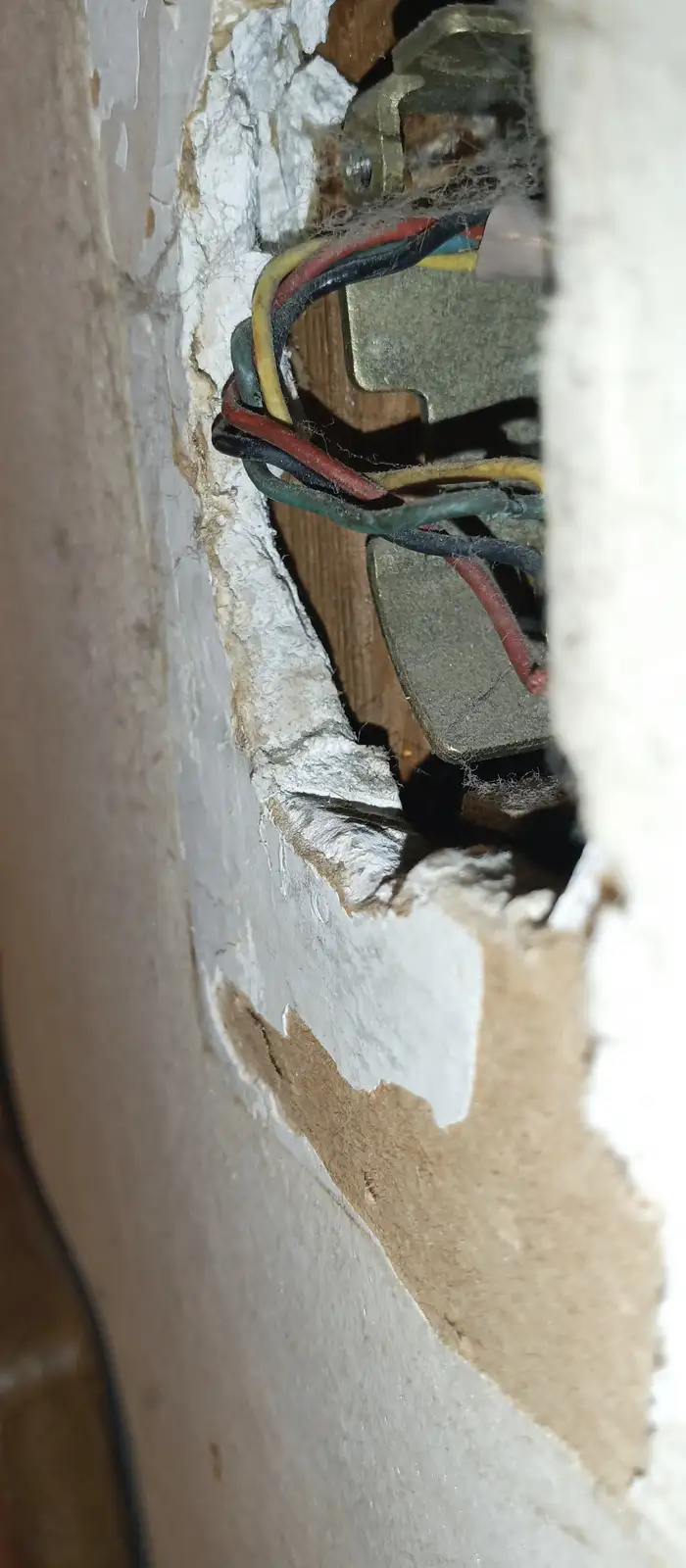 A close-up photo shows a jagged hole in a wall revealing exposed wiring, wooden framing, and cobwebs inside. The overlaid…