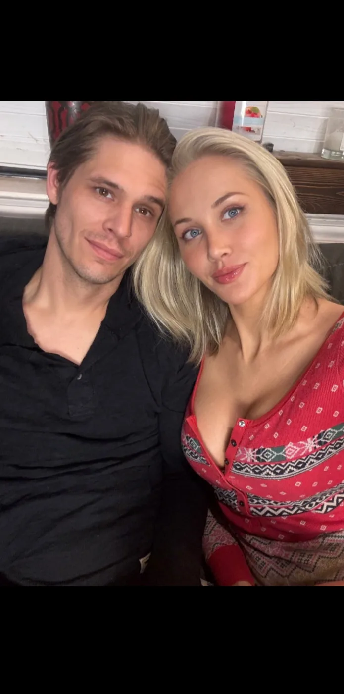 A selfie of a man and a woman sitting close together, the woman looking directly at the camera with a slight smile while the…
