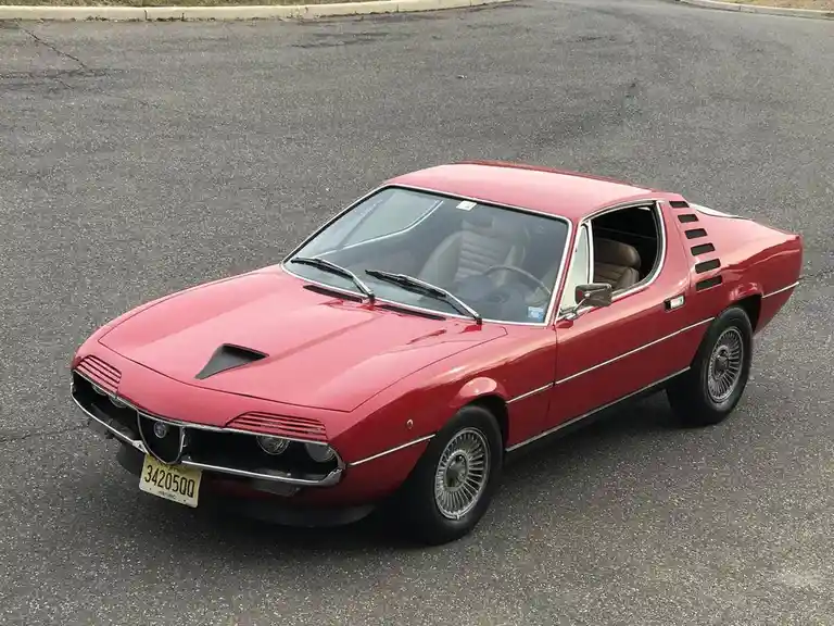 a red alfa romeo 33 stradale sports car is parked on asphalt, its driver's side door open, revealing the interior. The car…