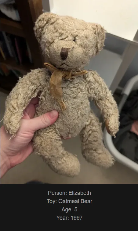 A hand holds a very old, worn, beige teddy bear with frayed fur and a faded bow. Text at the bottom identifies it as…