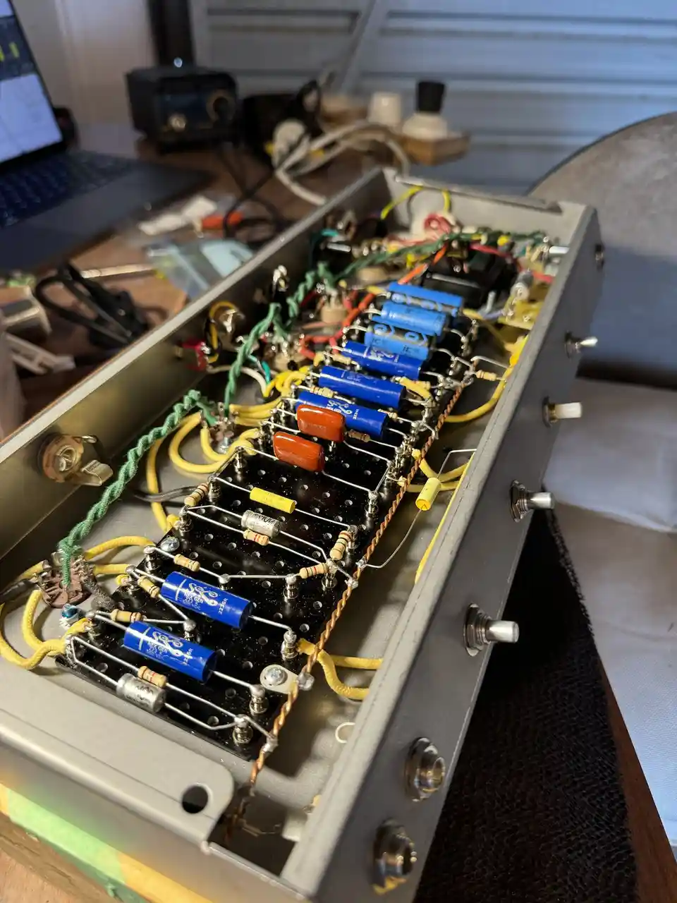 A close-up photo shows the open chassis of a custom-built electronic device, revealing a dense, hand-wired circuit board…