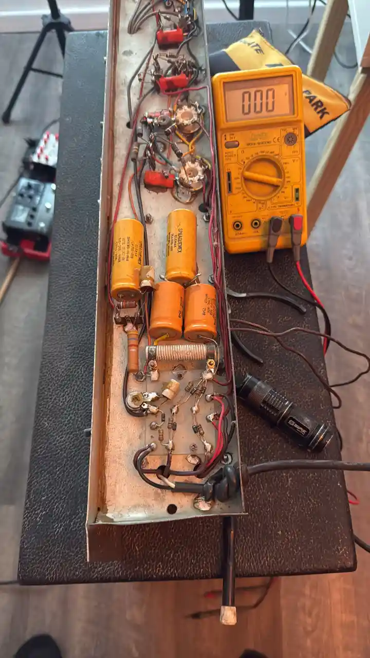 A close-up photo shows the exposed internal circuitry of a guitar amplifier, featuring orange capacitors, resistors, and…