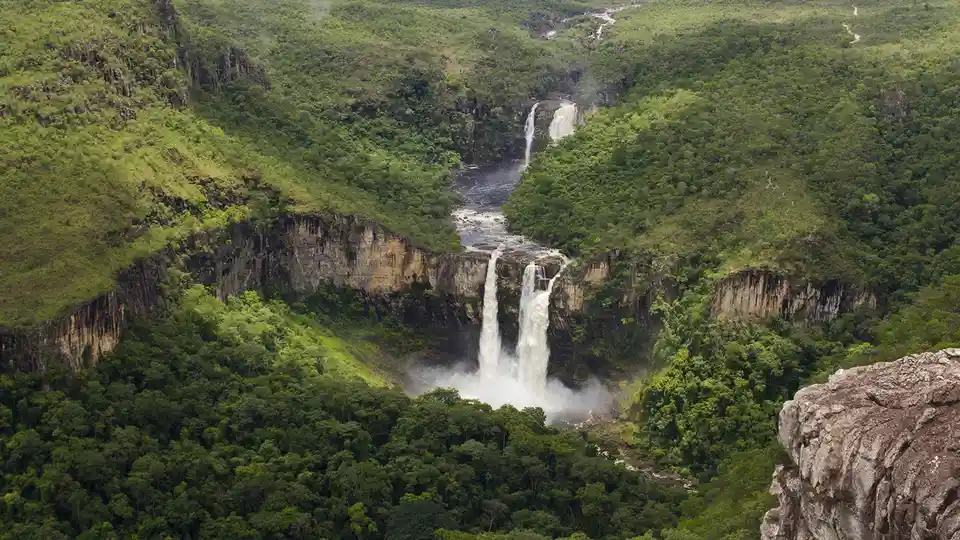 In northeastern Brazil's Chapada dos Veadeiros National Park, towering waterfalls cascade down cliffs beside a forested…