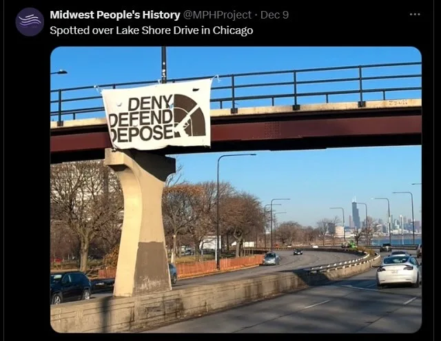 A white banner with bold black text reading 'DENY DEFEND DEPOSE' is hung from a bridge over a highway in Chicago, with cars…