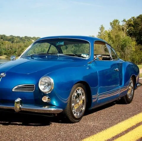 A shiny blue vintage Karmann Ghia sports car is parked on a road with trees in the background. The overlaid text reads 'i'm…