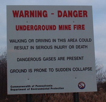 A white warning sign with red and black text warns of an underground mine fire in Pennsylvania, stating that walking or…
