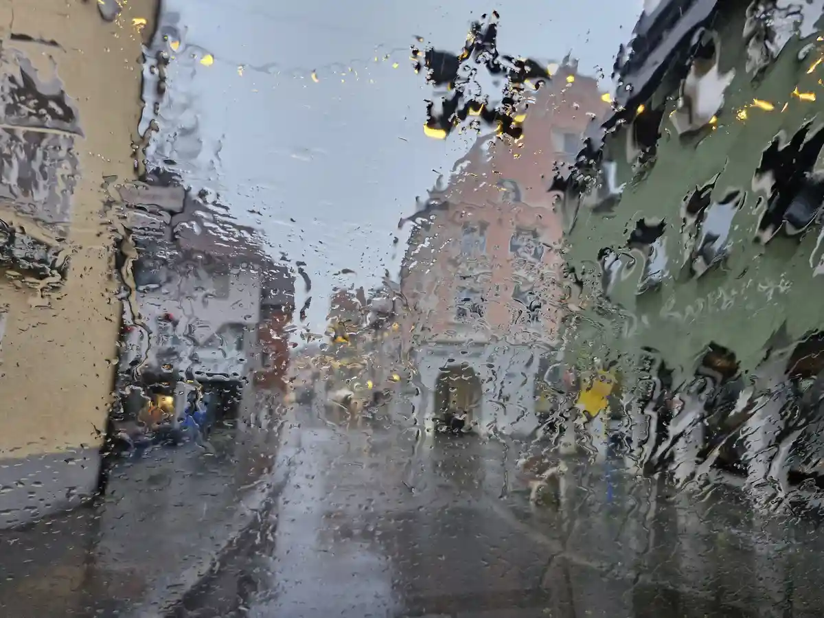 A blurry, rain-splattered view from inside a vehicle looking out at a city street, where water droplets distort the image of…