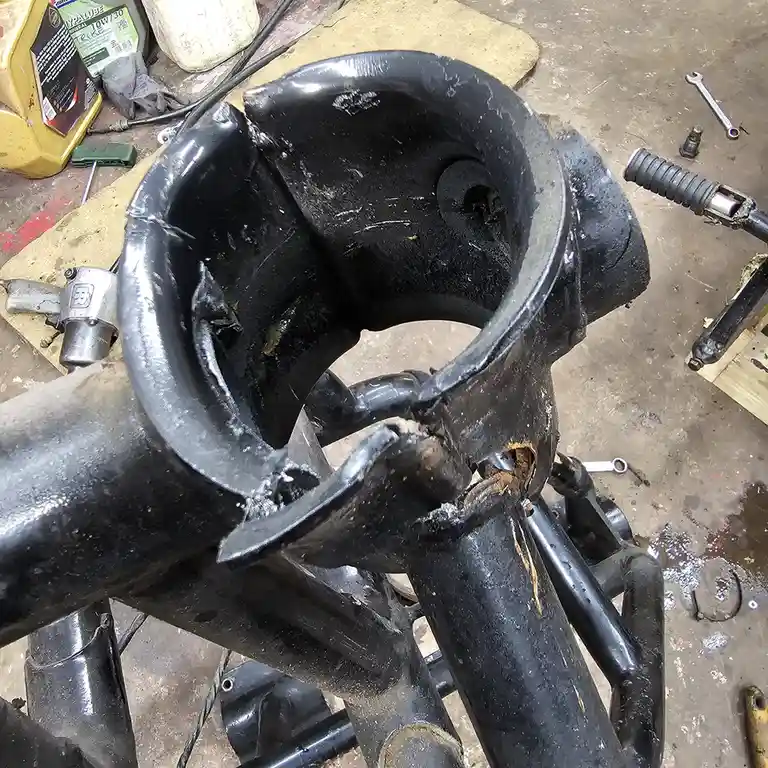 A close-up photo shows a heavily damaged, black-painted motorcycle frame with a large, jagged crack near the steering head…