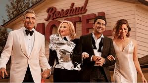 Four people, two men and two women dressed in formal wear, stand smiling in front of a building with a sign that reads…