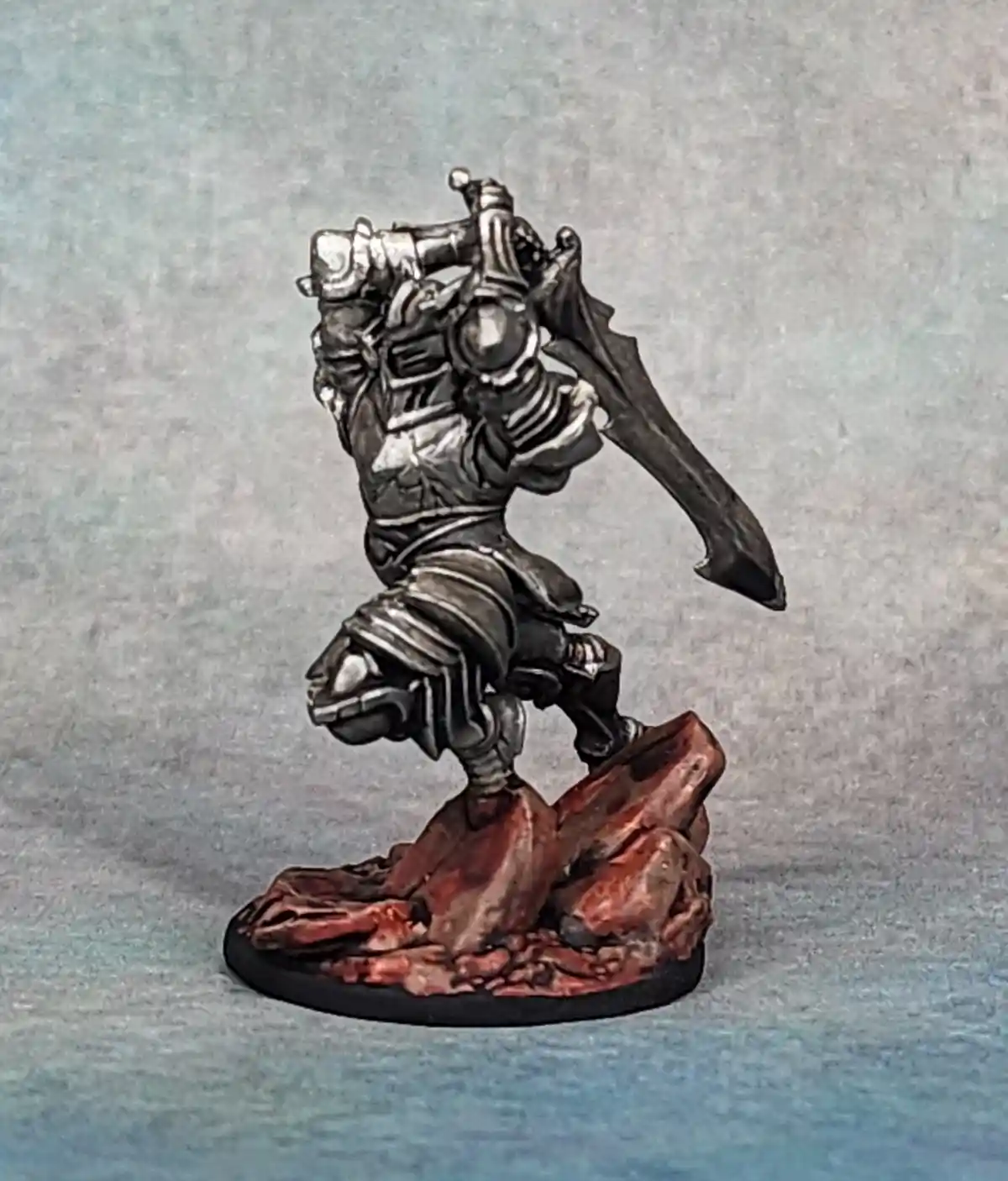 A painted miniature of a heavily armored warrior in a dynamic, aggressive pose, wielding a large sword and shield, standing…