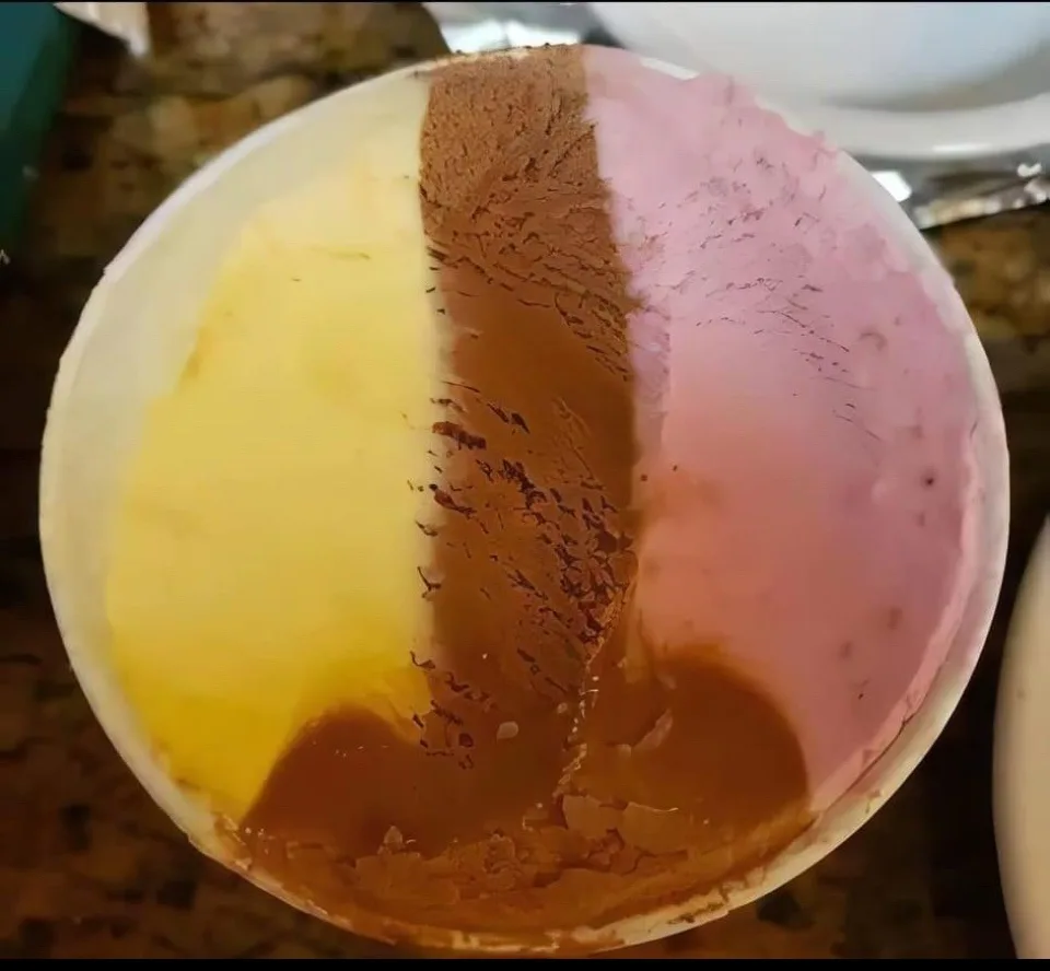A top-down view of a partially eaten ice cream container showing three distinct flavors: yellow vanilla, brown chocolate…