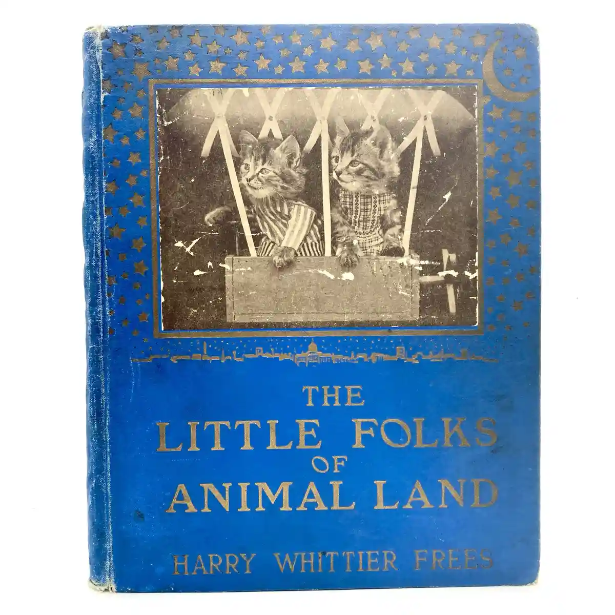 A vintage blue book cover with gold stars and a crescent moon, featuring a sepia-toned illustration of two kittens in a…