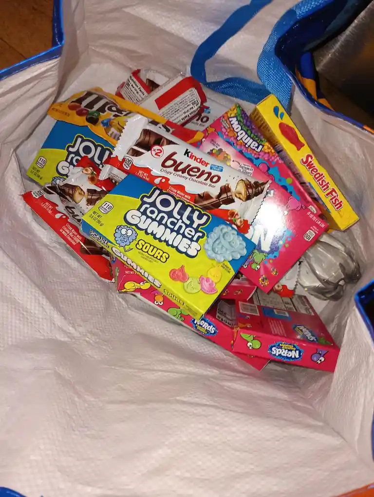 A white reusable shopping bag filled with various colorful candy packages including Jolly Rancher Gummies Sours, Kinder…