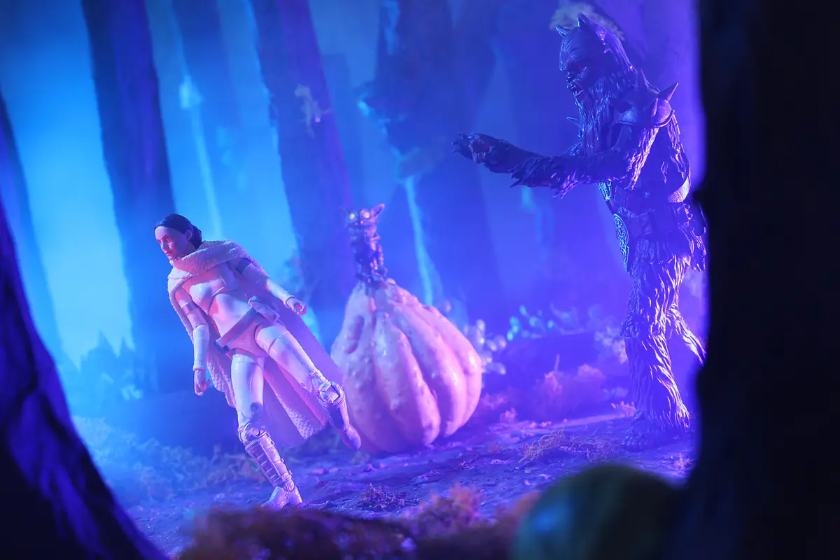 A staged scene with action figures: a female character in white armor and a furry cloak runs away from a menacing, horned…