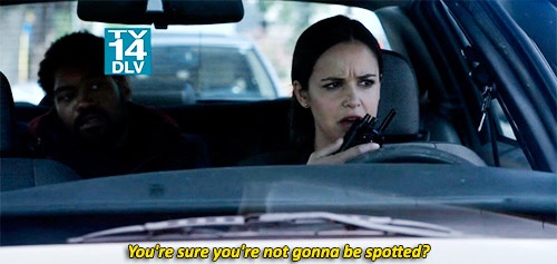 A woman in a car holds a walkie-talkie with a skeptical, worried expression while a man sits beside her. A TV-14 DLV rating…
