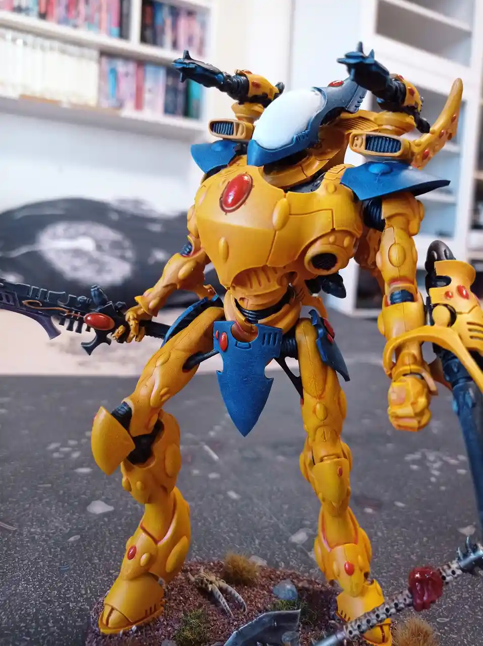 A yellow and blue painted Warhammer 40k Chaos Space Marine miniature stands in a dynamic pose, holding a weapon, with a…