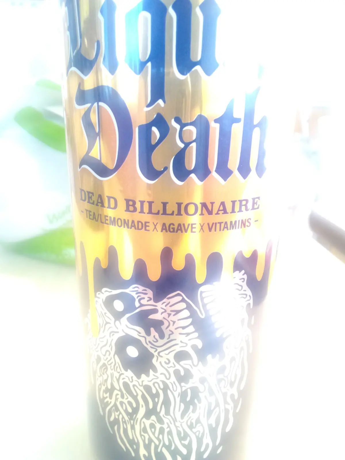 A close-up, overexposed photo of a beverage can labeled 'Liquor Death' with 'DEAD BILLIONAIRE' and ingredients 'TEA/LEMONADE…