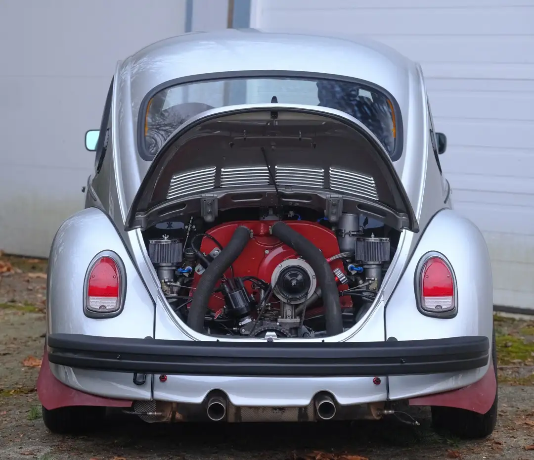 a silver volkswagen beetle with its rear engine compartment open, revealing a red custom engine with black hoses and…