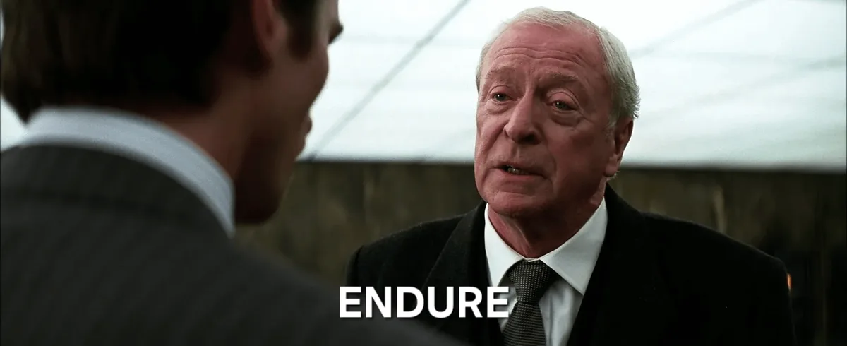 An older man in a dark coat and tie looks intently at another man in a suit, with the word 'ENDURE' overlaid in large white…