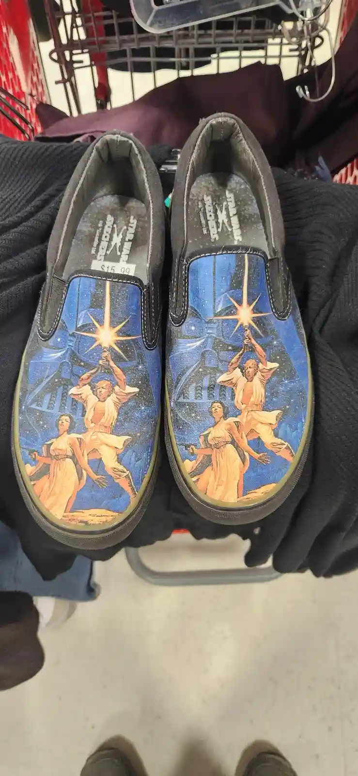 A pair of black slip-on shoes with a Star Wars-themed design, featuring Luke Skywalker and Princess Leia holding lightsabers…